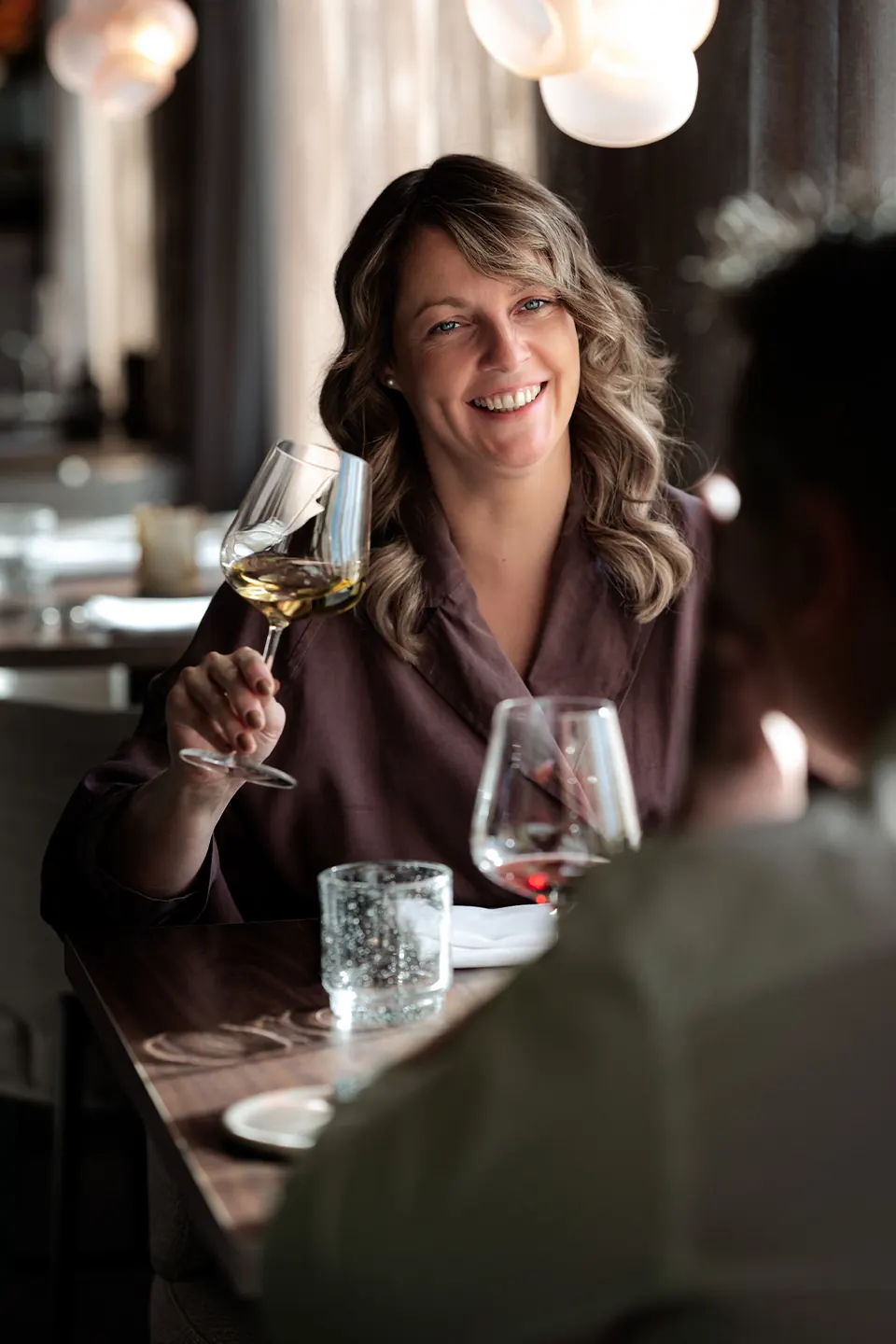 Een vrouw heft een glas witte wijn aan tafel met een metgezel