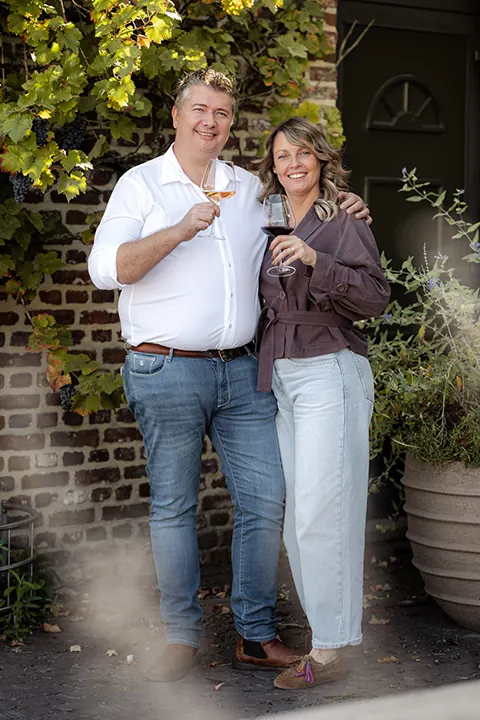 De oprichters van Vinoraya met een glas wijn bij een bakstenen gevel
